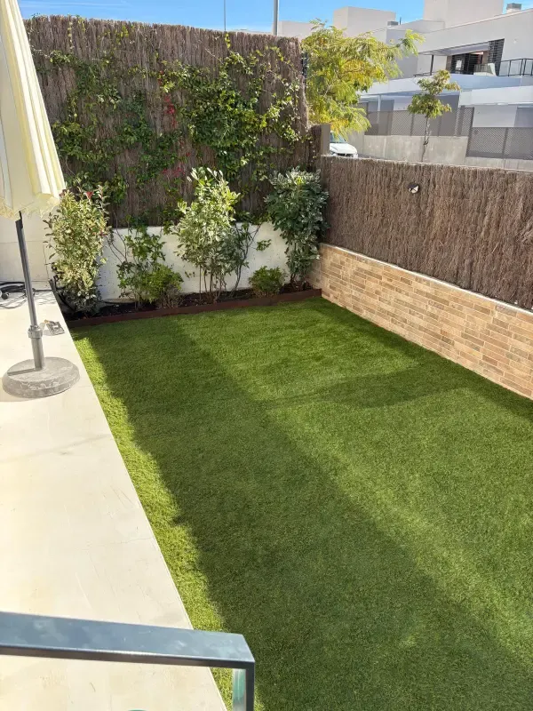 Jardín con césped artificial, jardineras y celosía de brezo